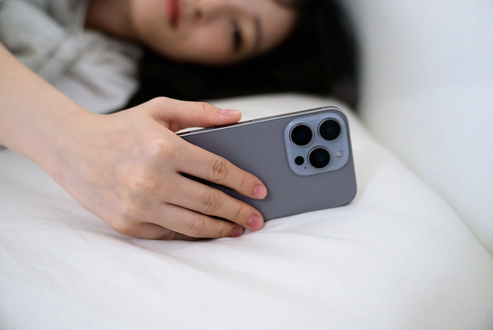 ベッドに横になりながらスマートフォンを見る人。
