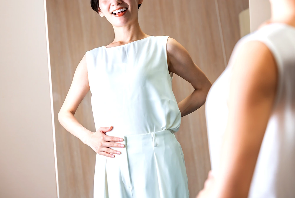 鏡の前でお腹に手を当てて体調を確認する女性。