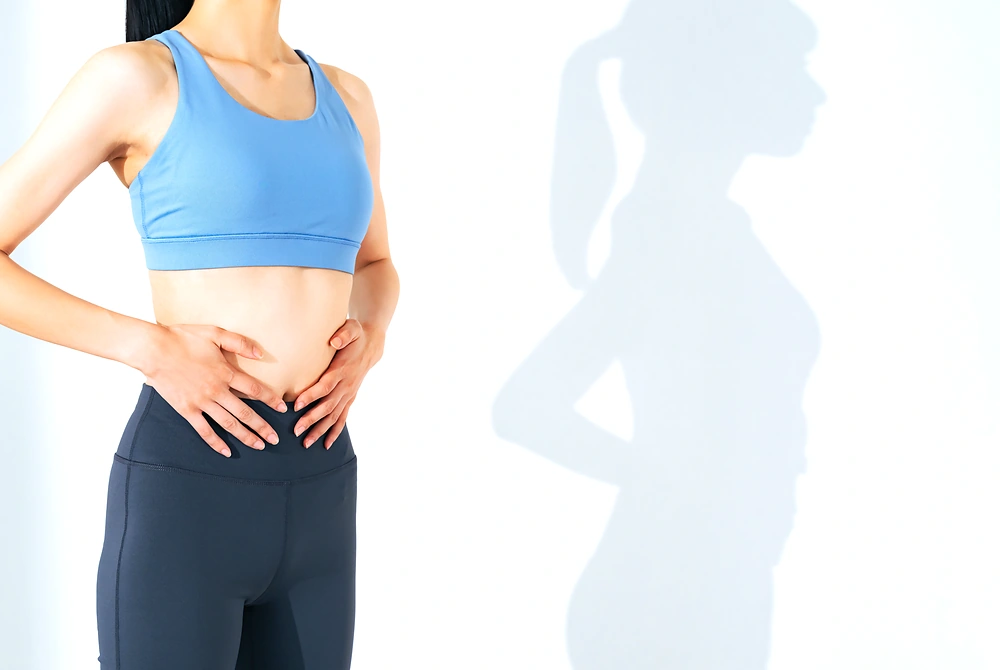 お腹に手を当てる女性と、体型の影のシルエット。