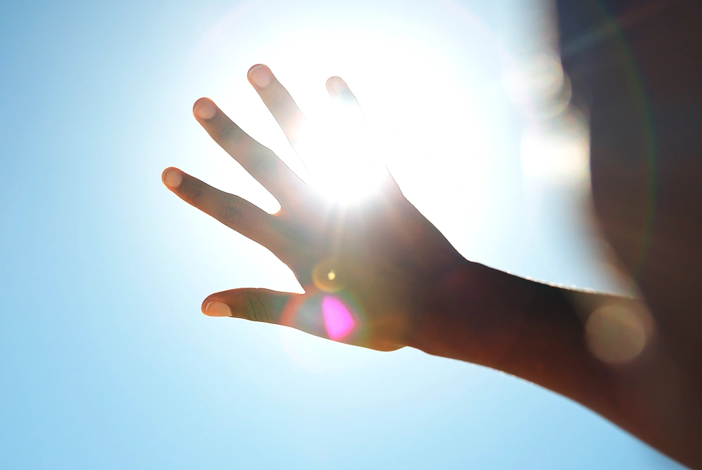 強い太陽の光を手で遮る様子。