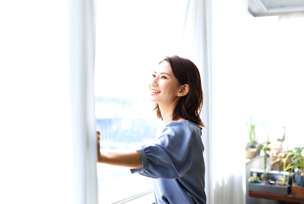 明るい室内で窓を開ける女性。