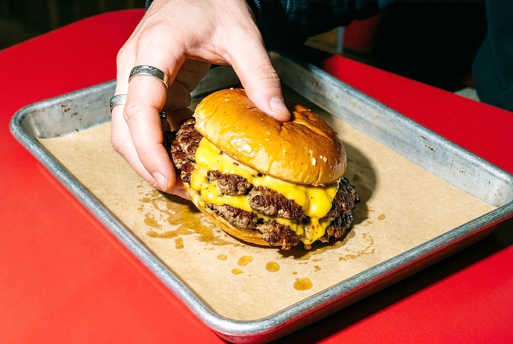 トレーに載ったチーズバーガーを手で持ち上げようとしている様子。