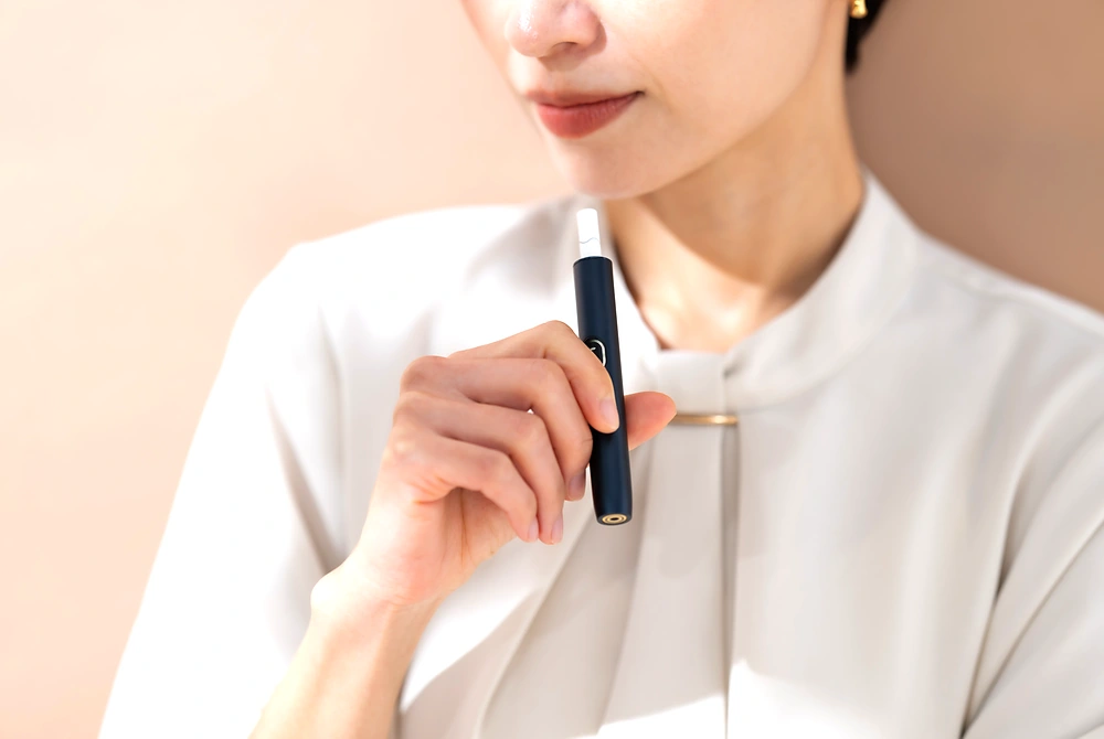 室内で電子たばこを手に持ち、口元に近づけている人。