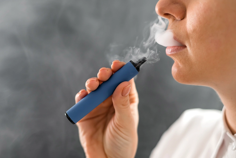 電子たばこを口にくわえ、煙状のエアロゾルを吐き出す人の口元。
