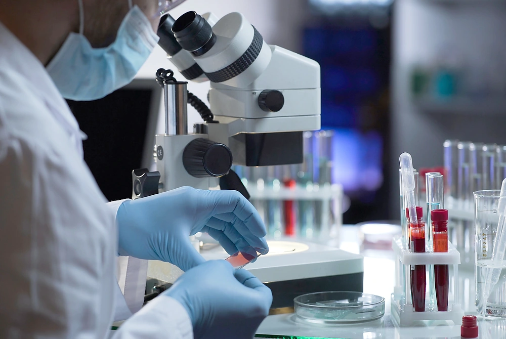 顕微鏡と試験管を使って、血液などの検体を調べる研究者の手元。