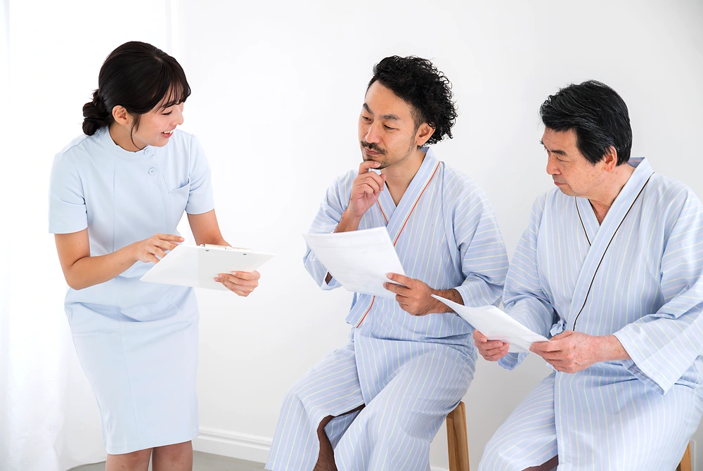 検査着姿の受診者2人に、医療従事者が書類を示して説明している様子。