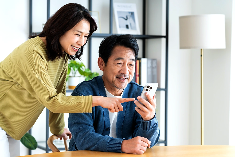 スマートフォンの画面を見ながら会話する中高年の男女。