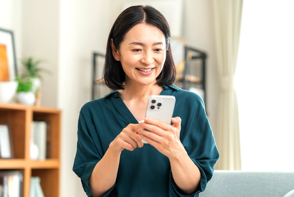 自宅でスマートフォンを操作する中年女性。