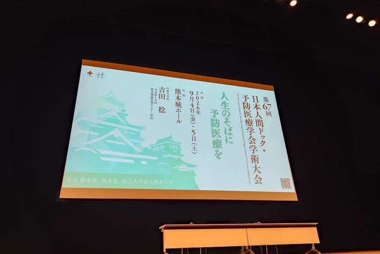 第67回日本人間ドック・予防医療学会学術大会の大会テーマと熊本城のイラストが表示された会場スクリーン。