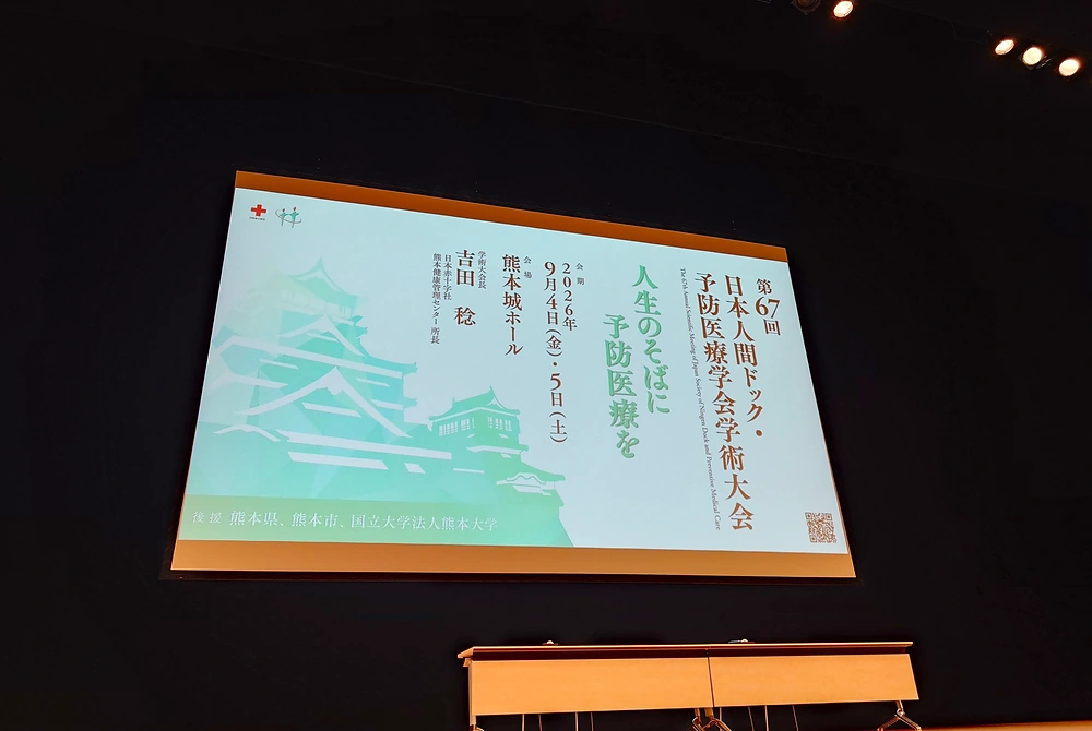 第67回日本人間ドック・予防医療学会学術大会の大会テーマと熊本城のイラストが表示された会場スクリーン。