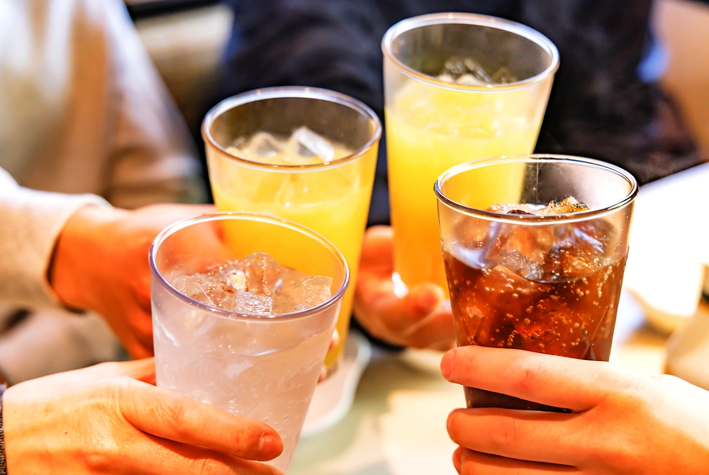 氷入りの清涼飲料が入った複数のプラスチックカップを持つ人たちの手元。