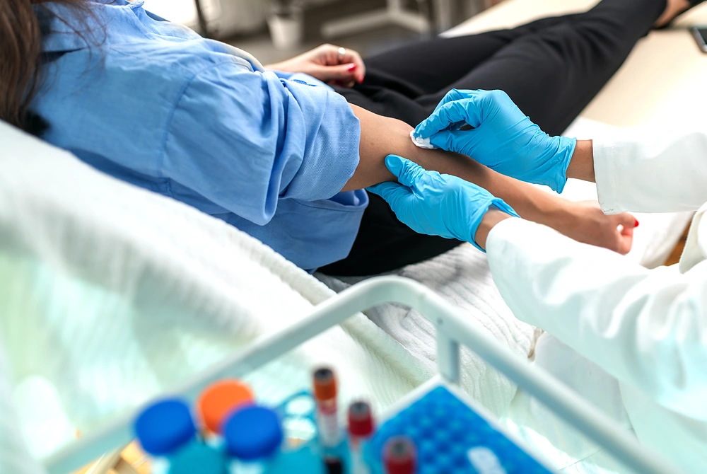 ベッドに横たわる受診者の腕から、医療者が採血している様子。