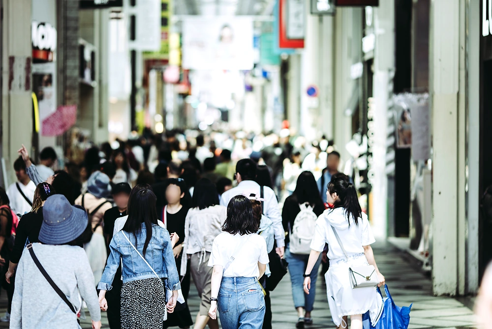商店街の通路を多くの人々が歩いている日常の街の風景。