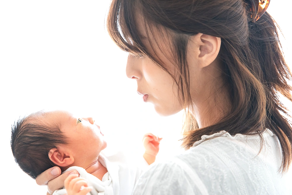 母親が新生児を抱き、顔を近づけて見つめている。
