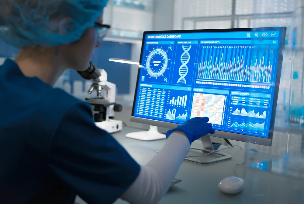 研究室でDNAの解析データを確認する研究者。モニターには遺伝子配列や解析結果を示すグラフが表示されている。