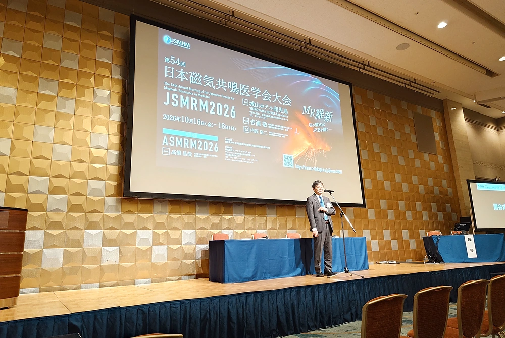 第54回日本磁気共鳴医学会大会の開会にあたり、大会長の吉浦敬氏がステージ上であいさつしている様子。