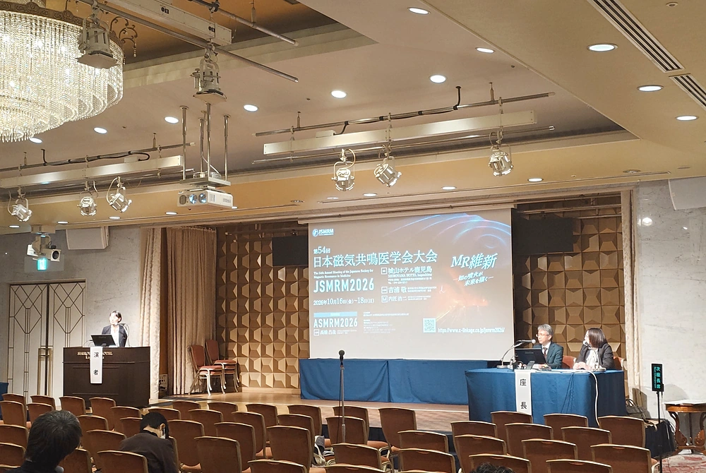 第54回日本磁気共鳴医学会大会のシンポジウム会場。演台で講演する登壇者と座長、講演を聴く参加者の様子。