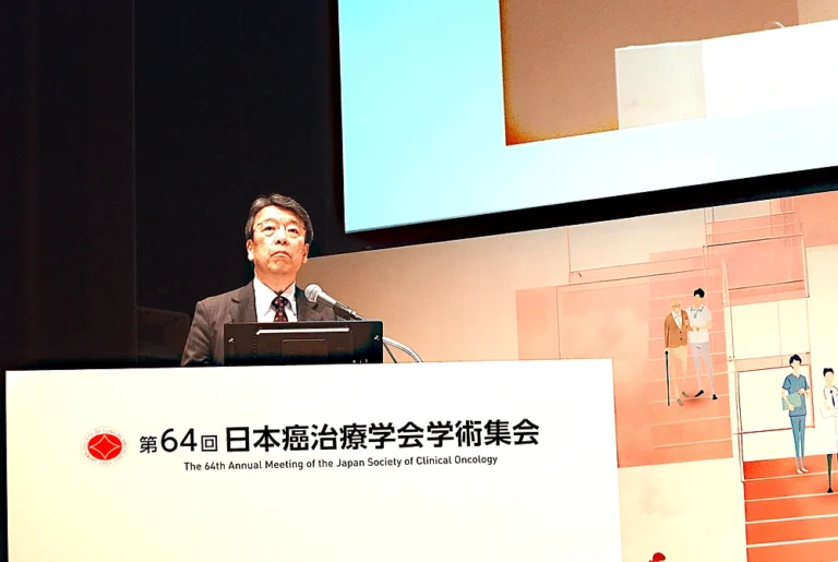 第64回日本癌治療学会学術集会の会長、河野浩二氏。大会名が記された演台で講演している様子。