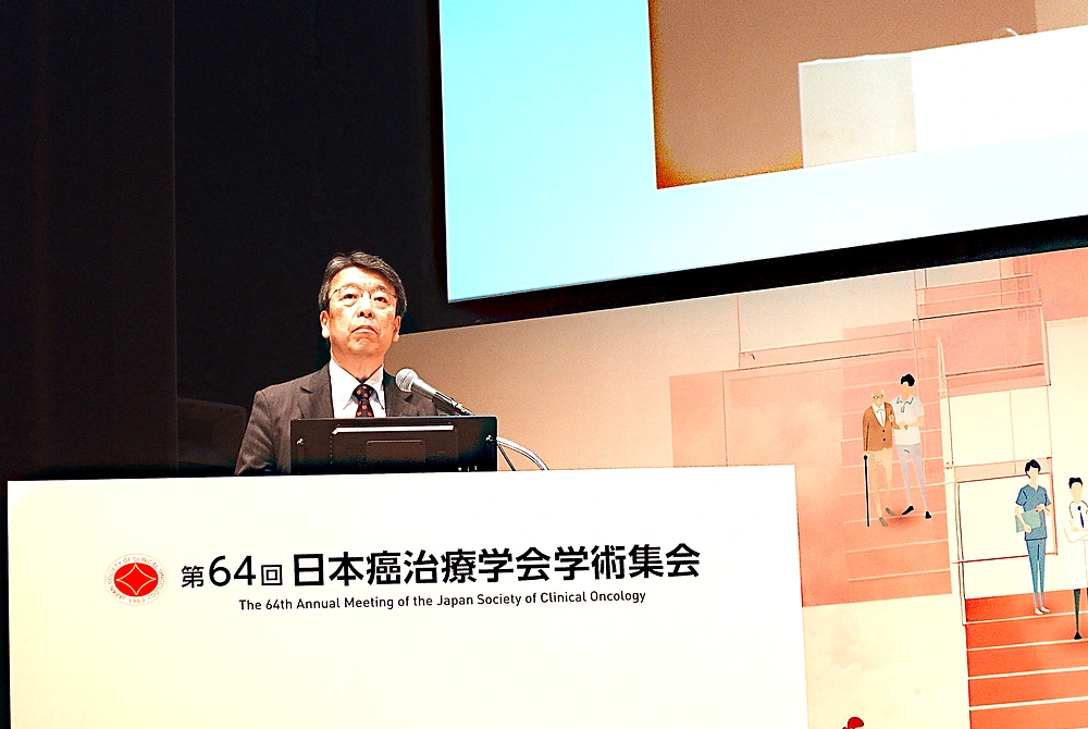 第64回日本癌治療学会学術集会の会長、河野浩二氏。大会名が記された演台で講演している様子。